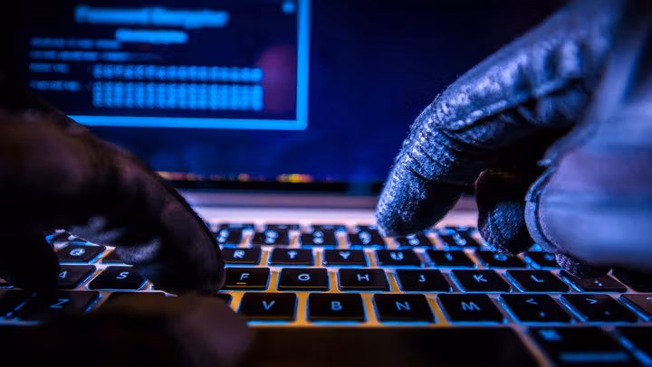Close up of hands typing on a keyboard in a darkened room.